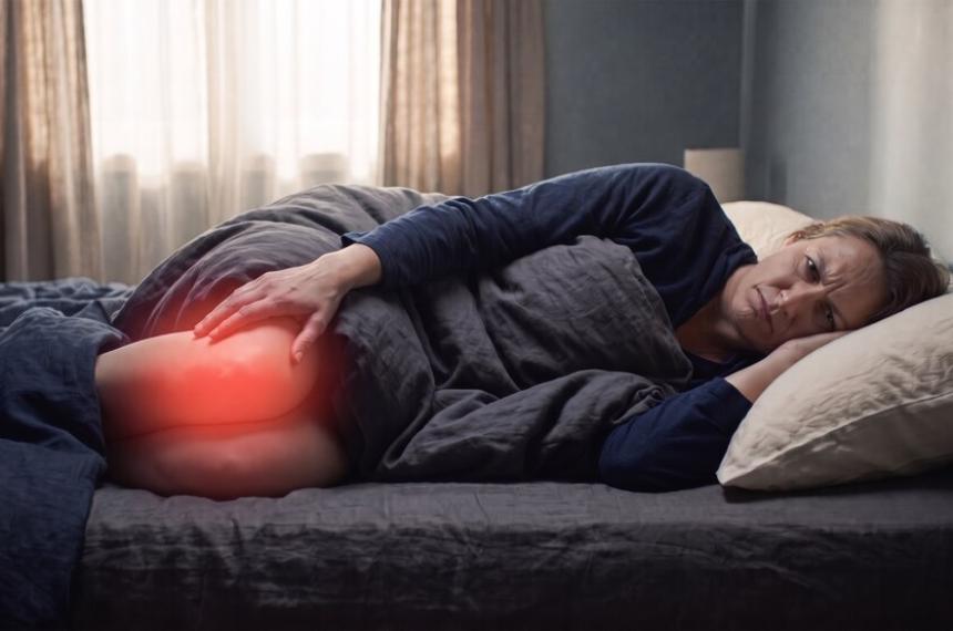 Una mujer recostada en la cama sostiene su pierna iluminada con una luz roja que representa dolor o inflamación