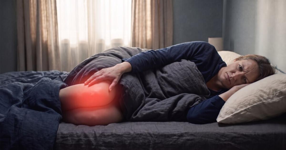 Una mujer recostada en la cama sostiene su pierna iluminada con una luz roja que representa dolor o inflamación